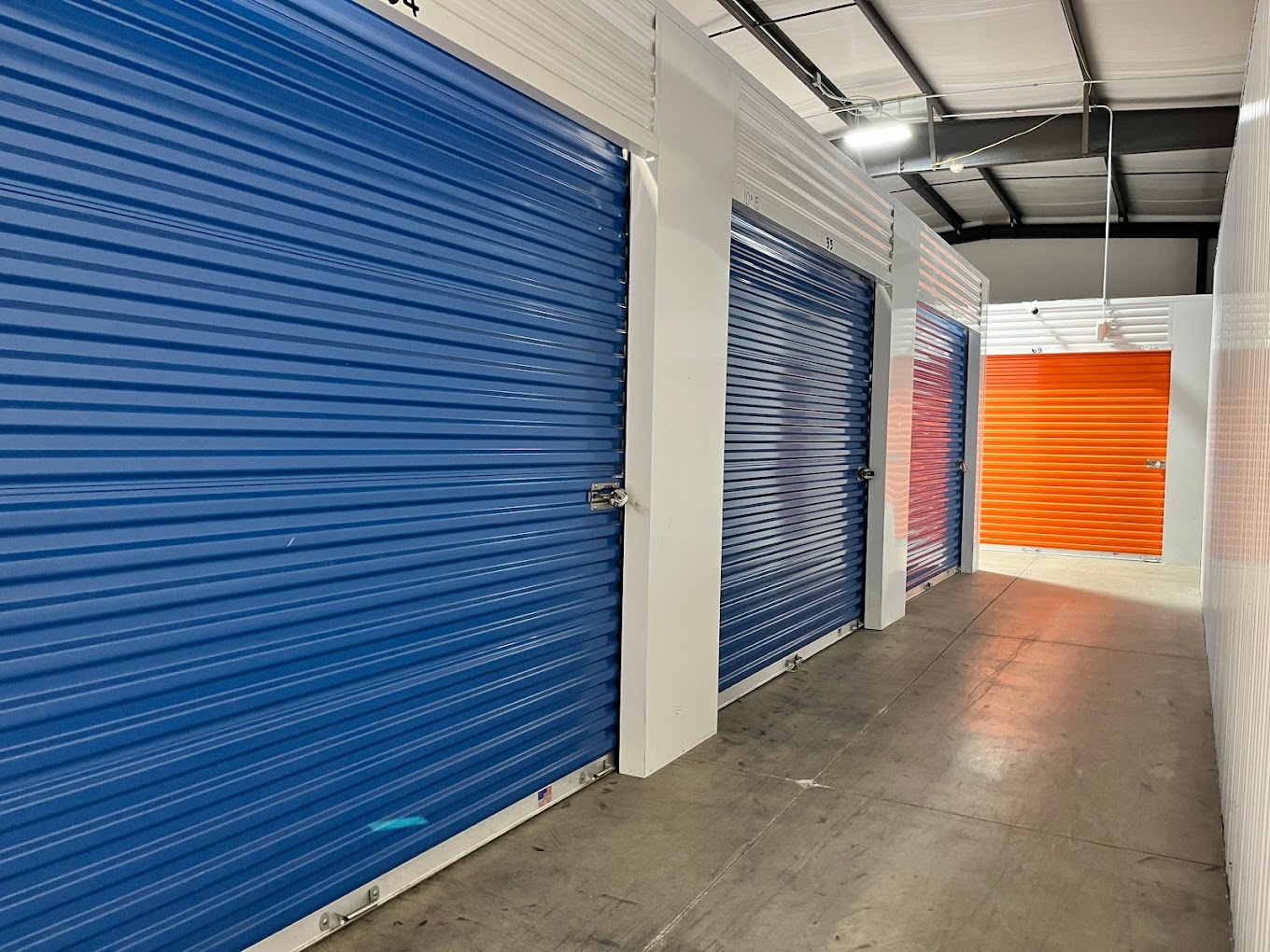 Indoor hallway of blue and orange roll-up unit doors at Storage Park 2nd St