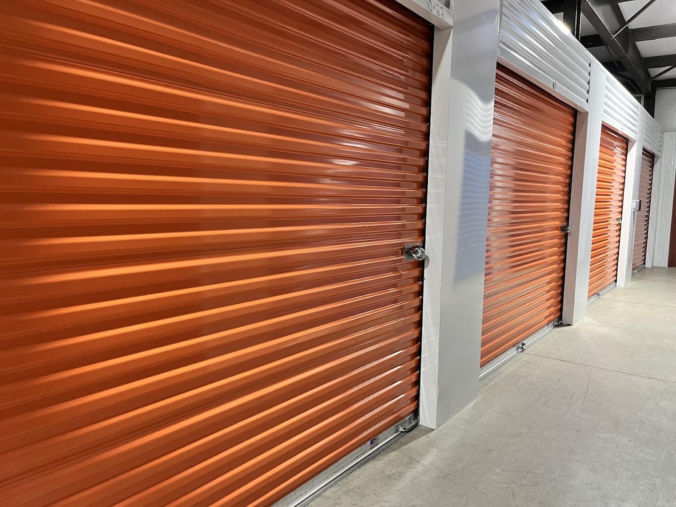 Row of indoor storage units with orange roll-up doors at Storage Park 2nd St